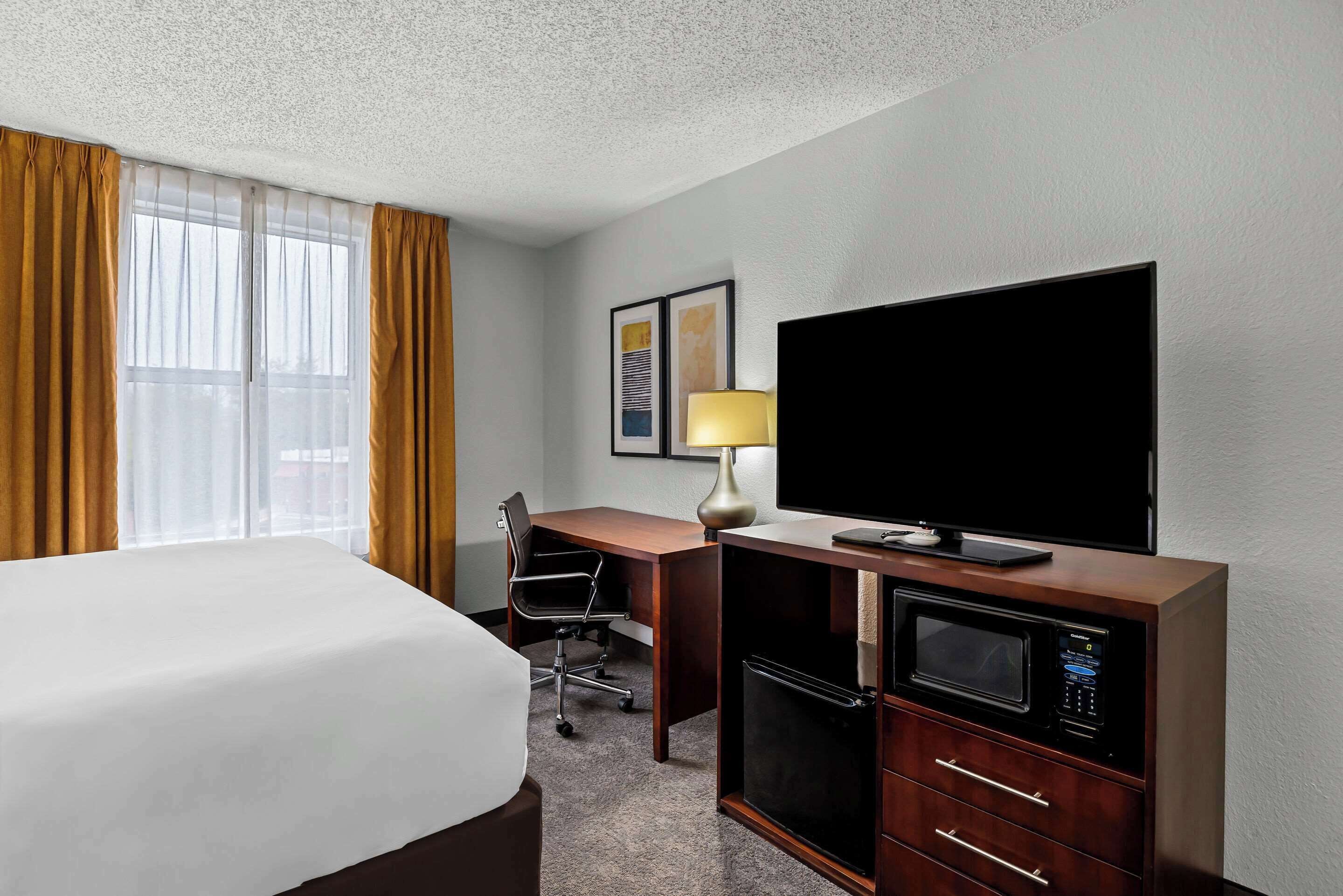Una habitación de hotel con cama, escritorio, televisión y microondas.