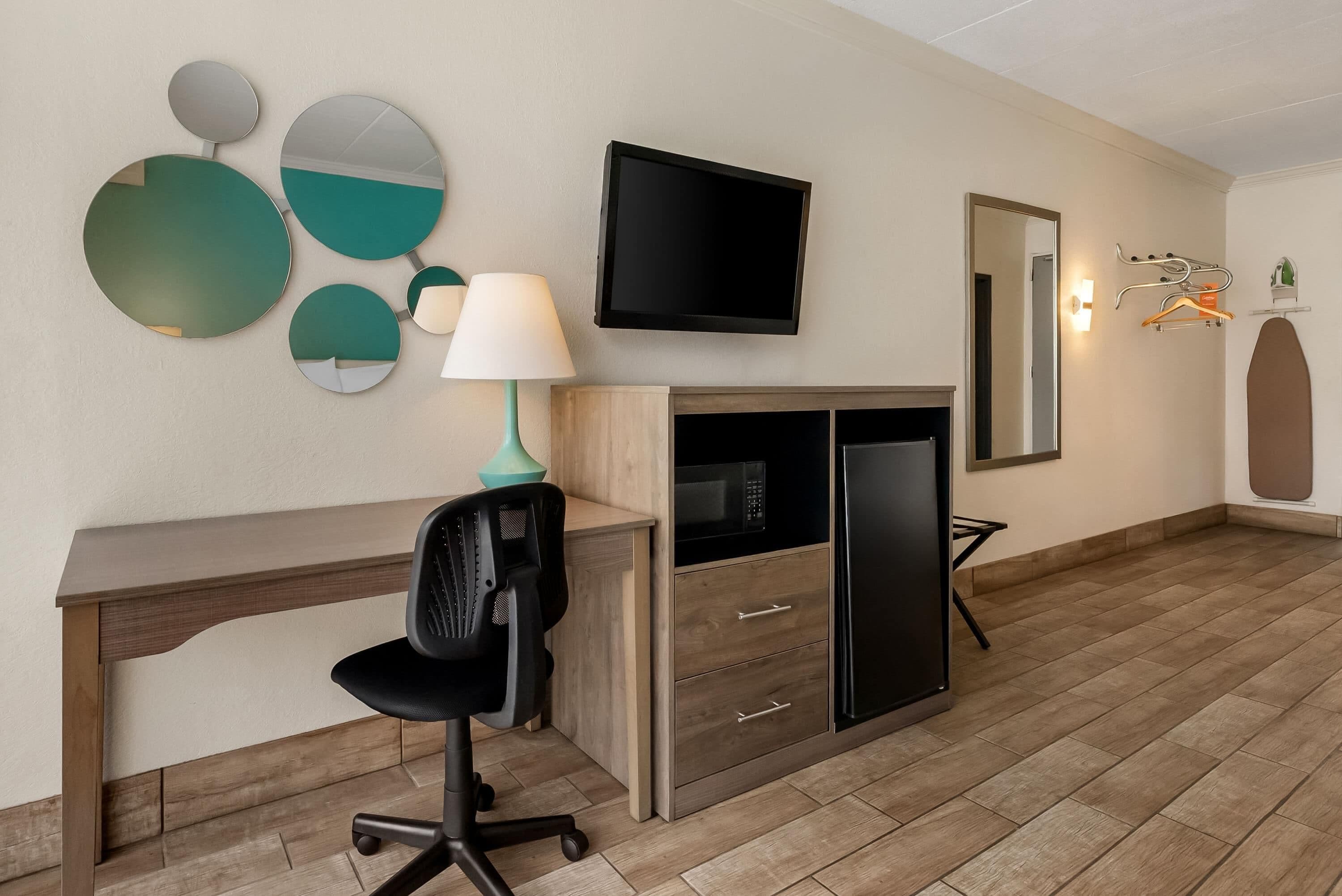 Habitación de hotel con escritorio, silla, televisor, espejo y microondas.