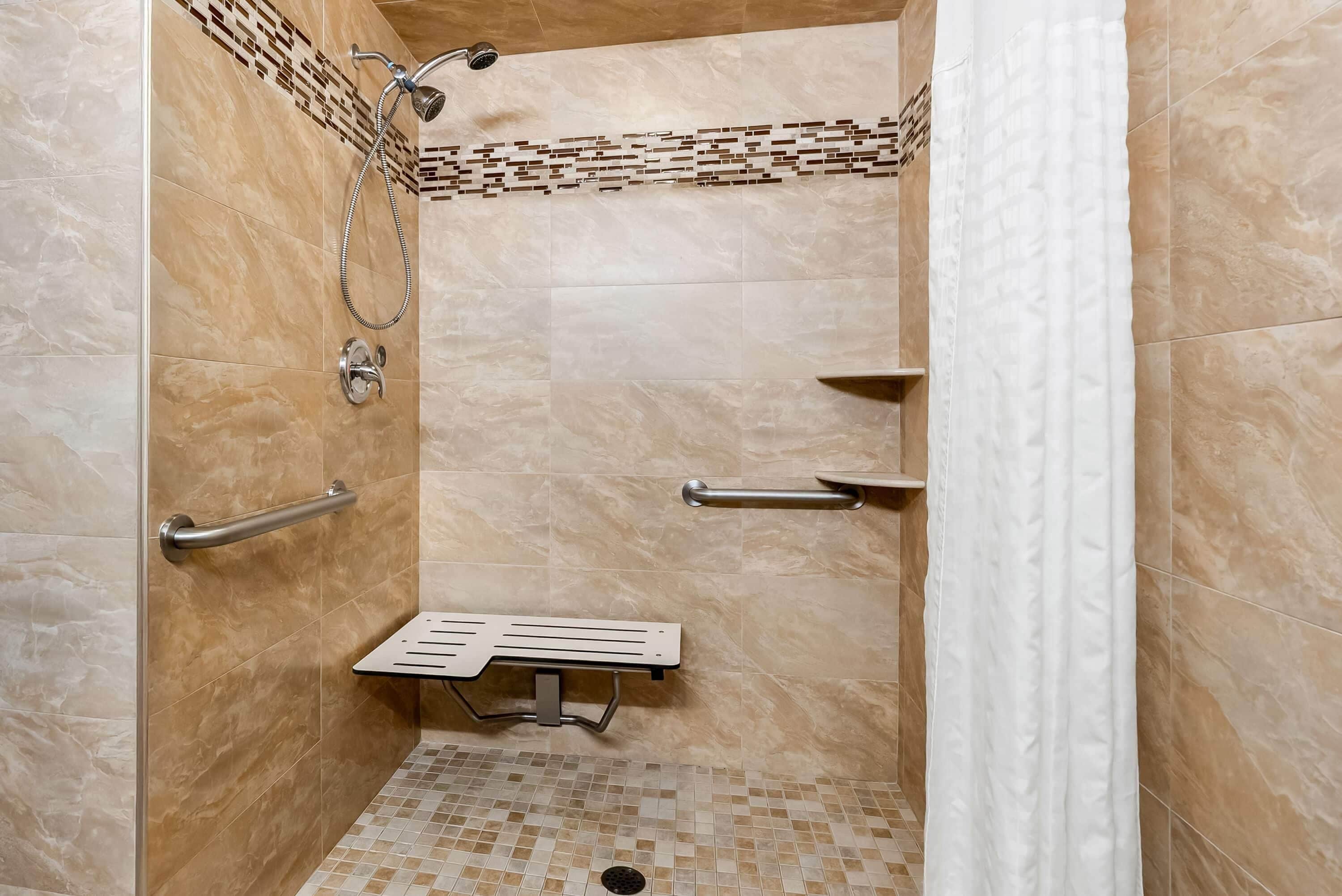 A shower stall with a handheld showerhead, a handheld shower attachment, a grab bar, and a small shelf.