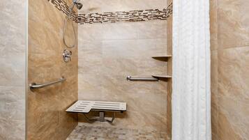 A shower stall with a handheld showerhead, a handheld shower attachment, a grab bar, and a small shelf.
