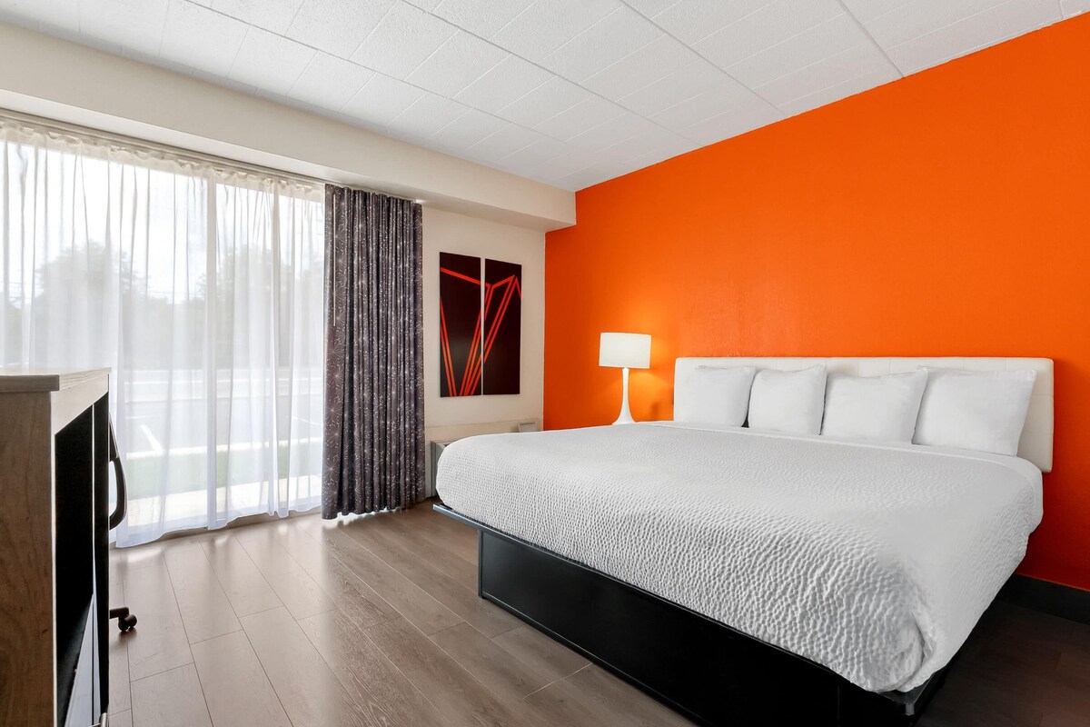 A hotel room with a bed, a desk, a lamp, and a window with curtains.