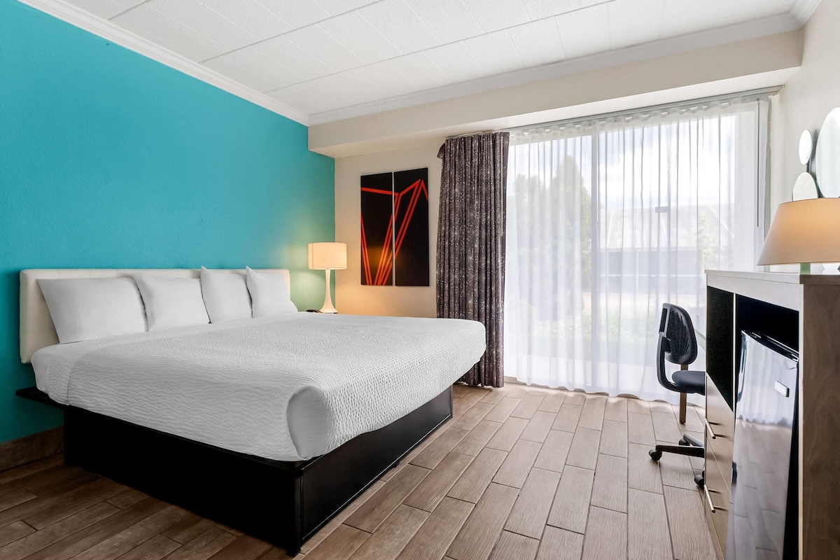 A hotel room with a bed, desk, chair, and a large window with curtains.