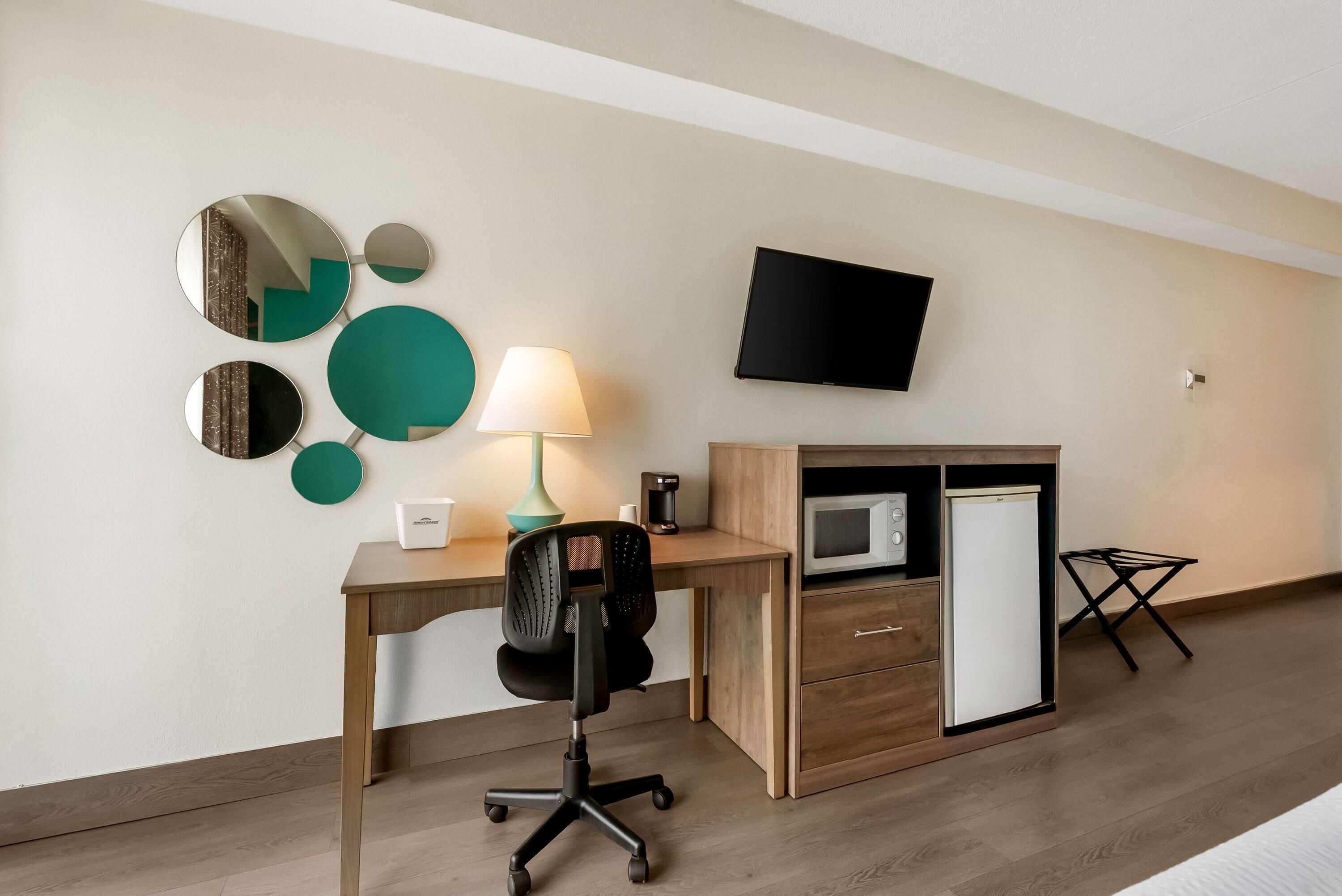 Habitación de hotel con escritorio, silla, televisor, microondas y refrigerador.
