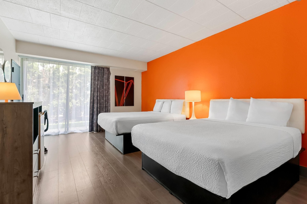 A hotel room with two beds, a desk, a lamp, and a window with curtains.