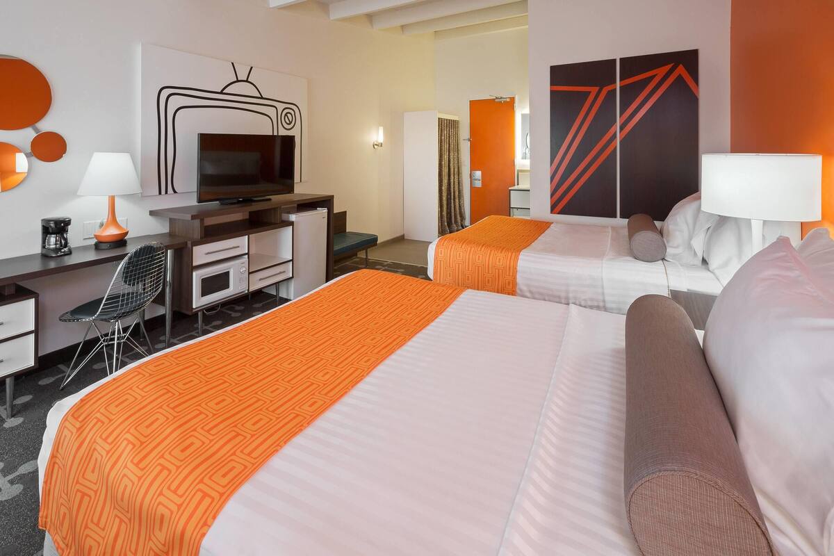 Une chambre d’hôtel avec deux lits, un bureau avec une télévision, une chaise et une salle de bain visible à travers une porte ouverte.