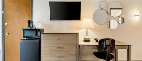 Quarto de hotel com televisão de tela plana, escrivaninha com cadeira, micro-ondas e geladeira.