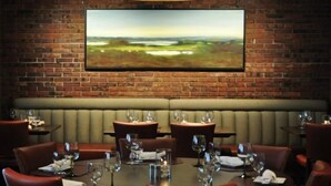 A restaurant with brick walls, a large painting, and leather booths.