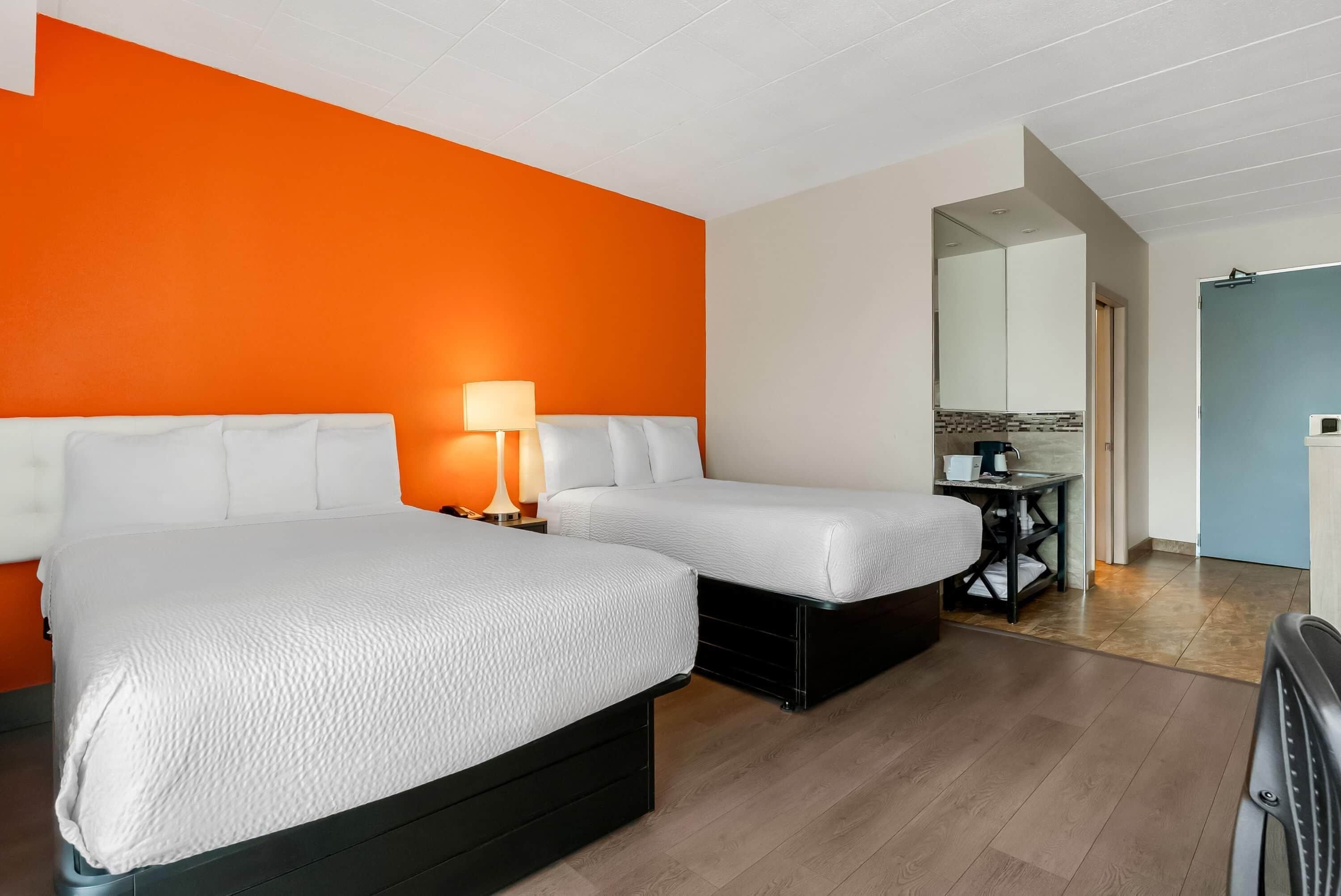 A hotel room with two beds, a nightstand with a lamp, a small table with a sink, and a mirror.