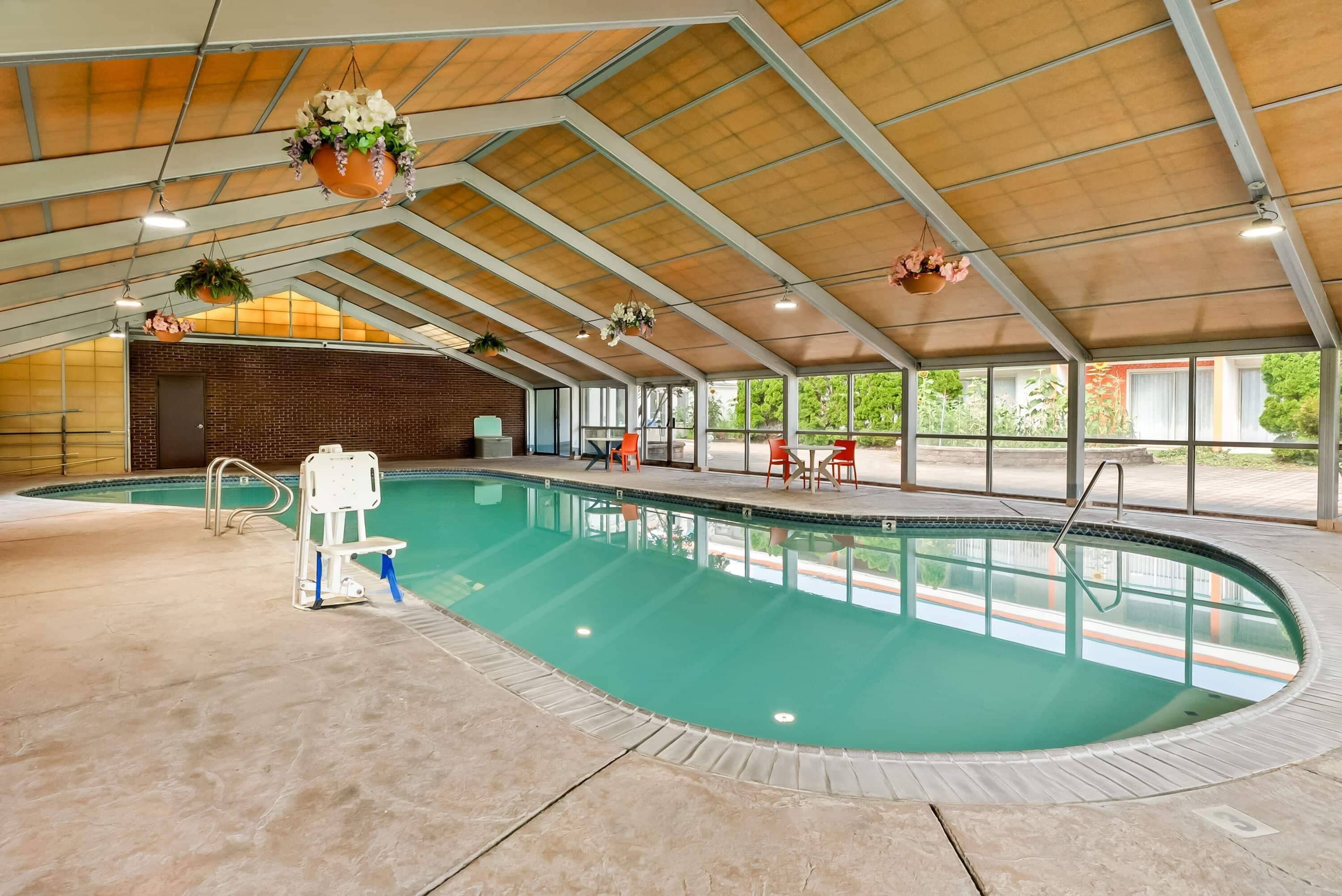 An indoor swimming pool with a high ceiling, a diving board, and a seating area with chairs.