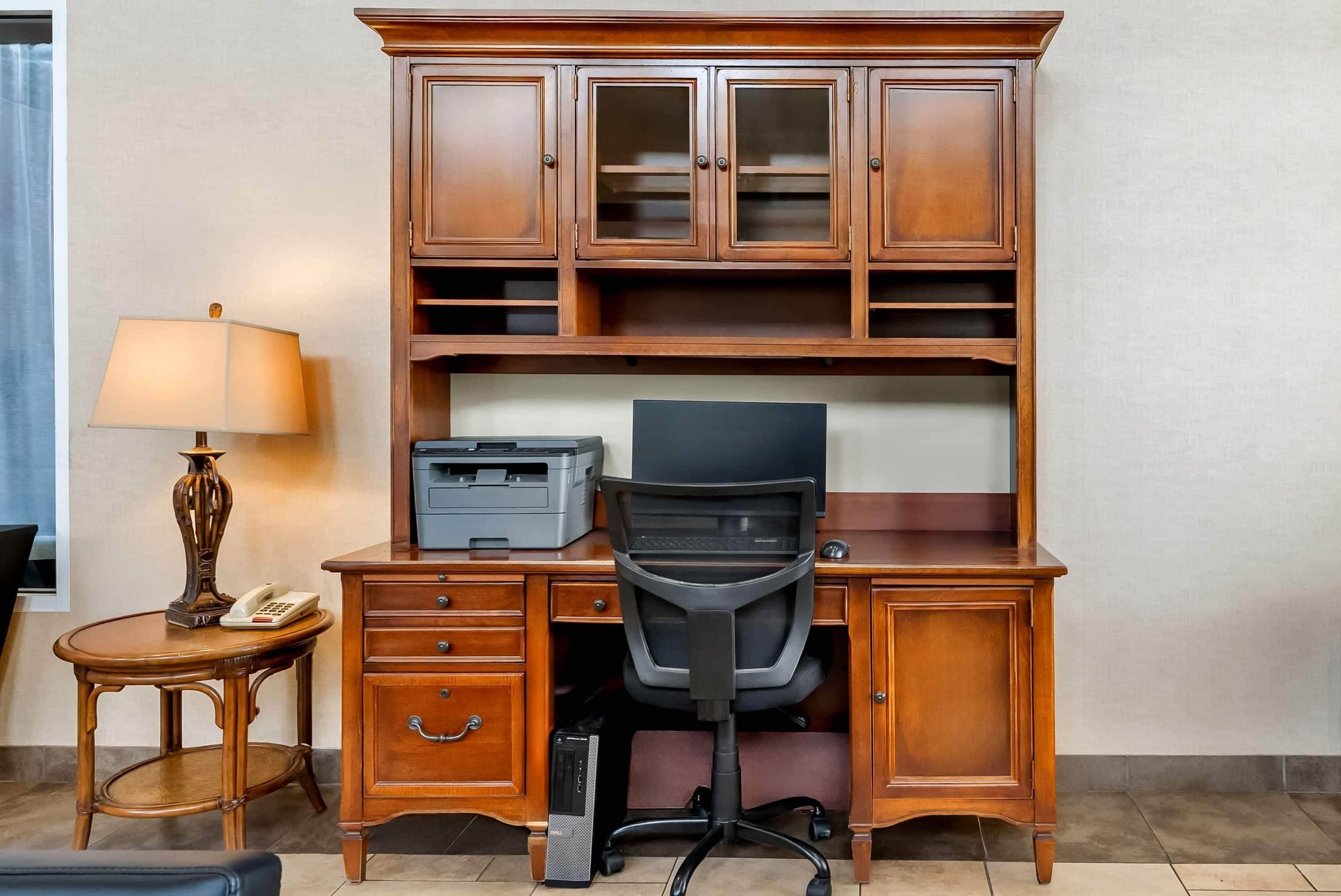 A wooden desk with a printer, a chair, and a lamp.