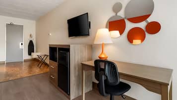 Et moderne hotelværelse med et fladskærms-TV, et skrivebord med stol, en lampe og et spejl monteret på væggen.