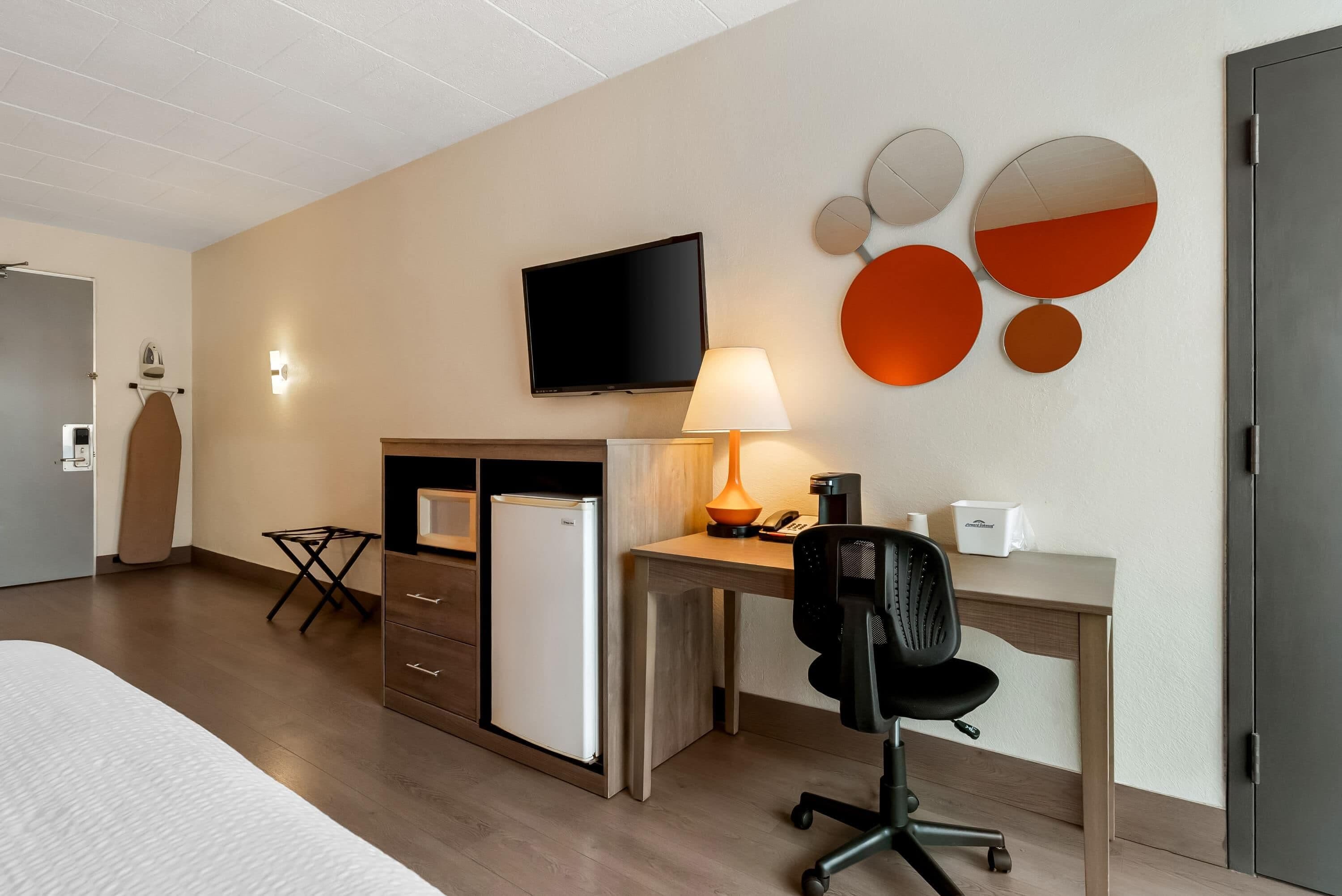 A hotel room with a bed, a desk, a chair, a television, a lamp, a coffee maker, a phone, and a wall with circular mirrors.
