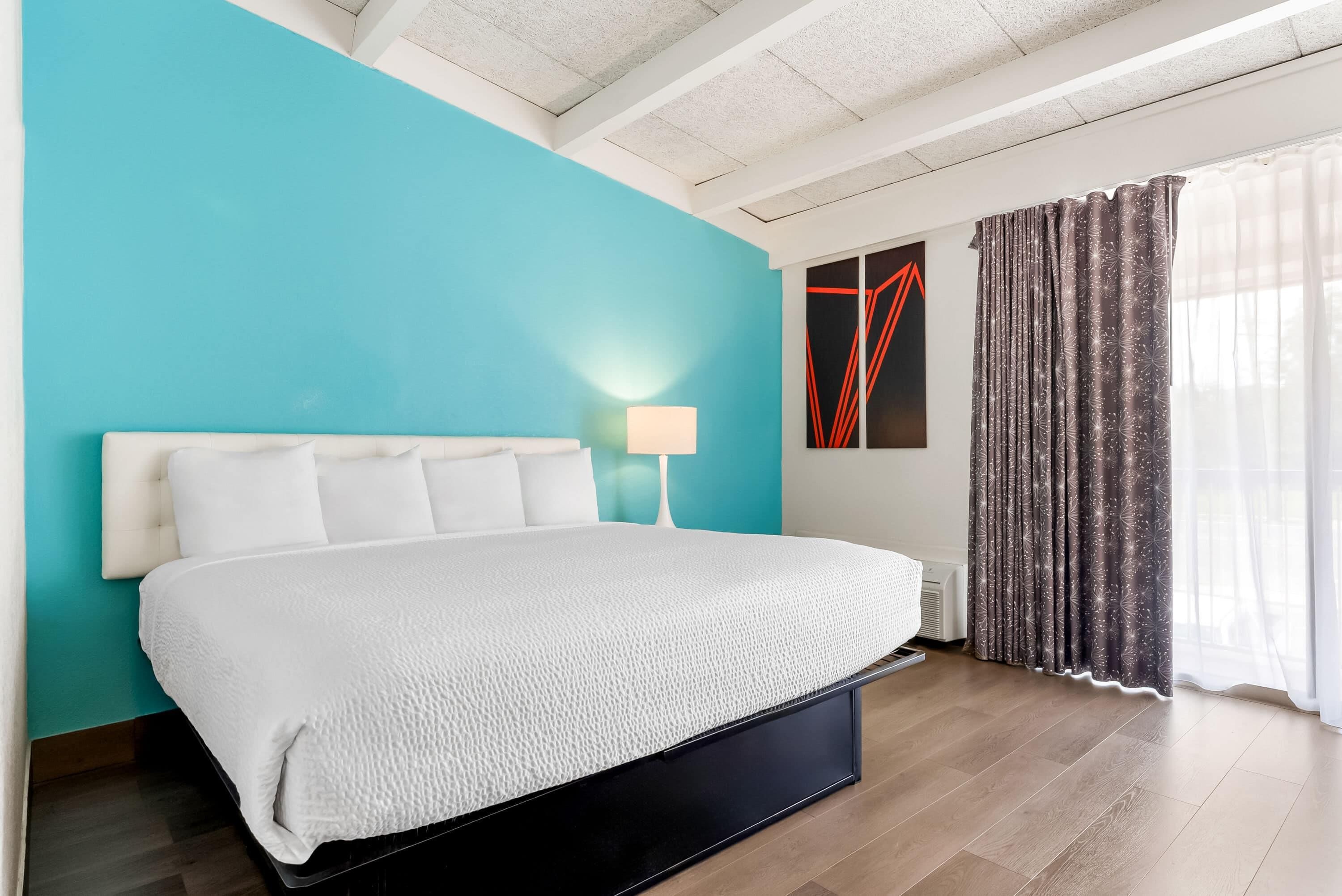 Ein modernes Schlafzimmer mit einem großen Bett, einem Nachttisch, einer Wandlampe und einem Fenster mit Vorhängen.