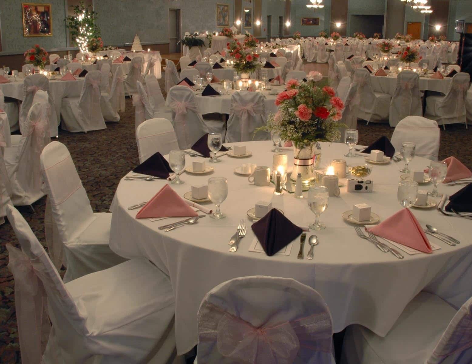 A banquet hall with round tables set for a formal event, adorned with floral centerpieces and candles.