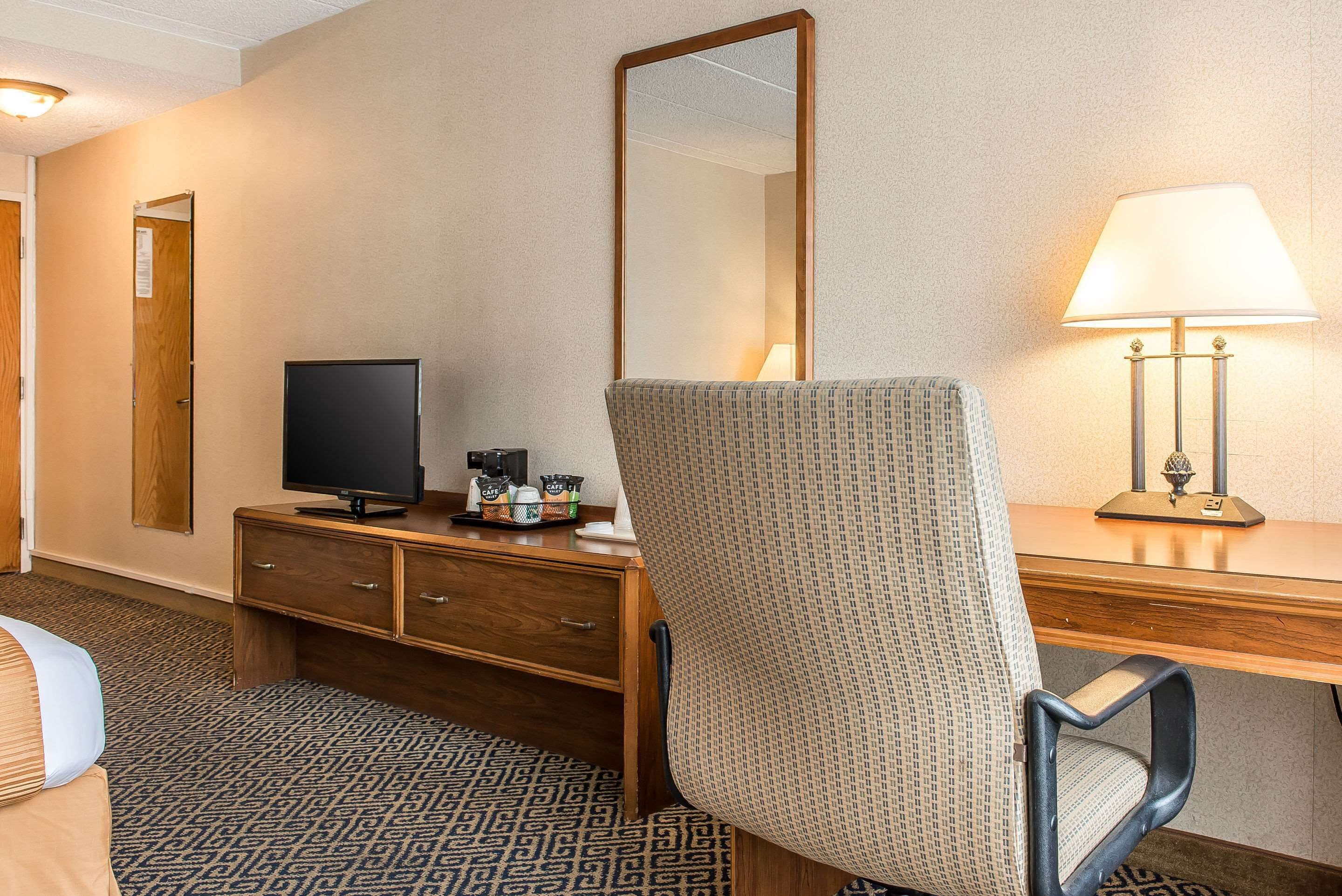 A hotel room with a bed, a desk with a lamp, a television, and a mirror.
