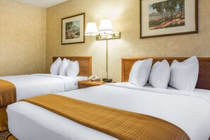 A hotel room with two beds, a nightstand with a phone and a remote, and wall-mounted lamps.