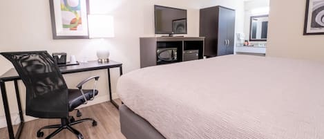 Una camera d'albergo con un letto, una scrivania, una sedia, una televisione e degli armadi.