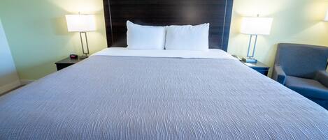 Una habitación de hotel con una cama grande, dos mesitas de noche con lámparas y una silla.
