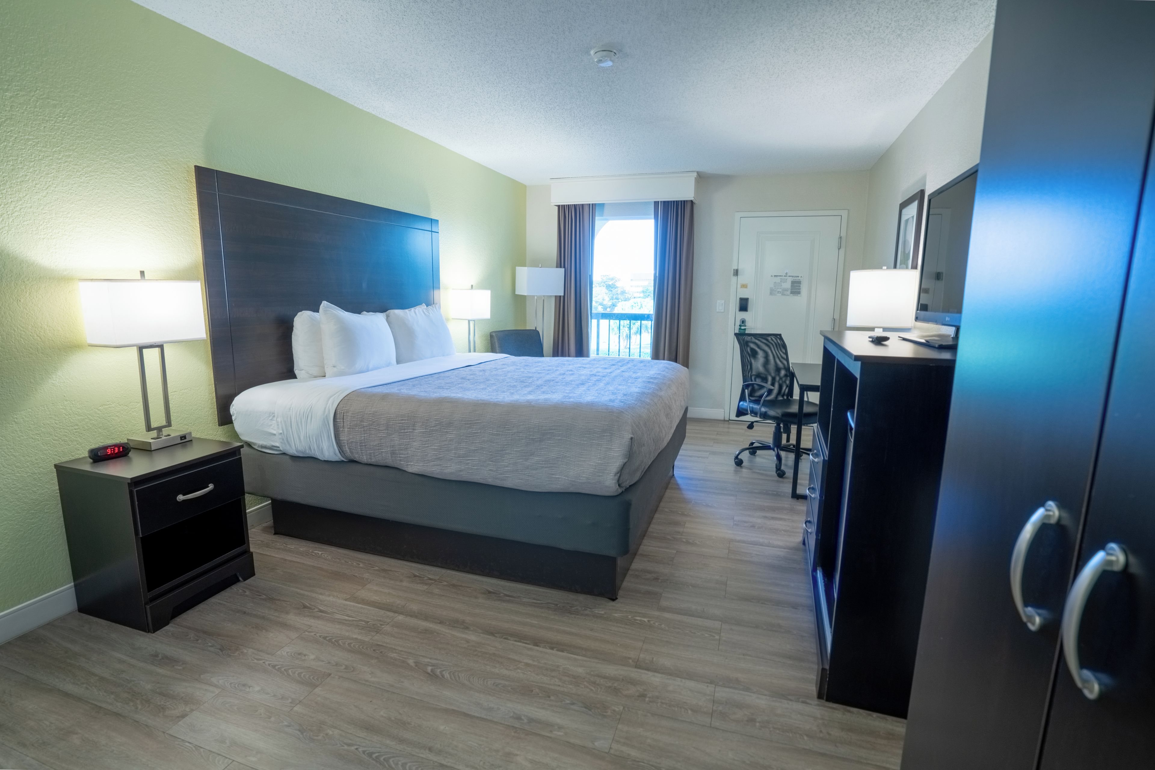 A hotel room with a bed, bedside tables, a desk with a computer, and a wardrobe.