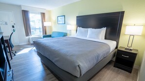 A hotel room with a large bed, a desk, a chair, and a bedside table with lamps.