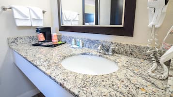 Un baño con lavamanos de encimera de granito, un secador de pelo y un espejo sobre el lavamanos.
