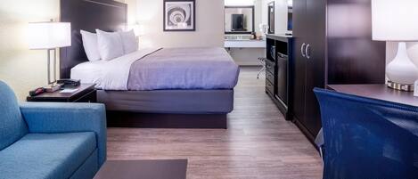 A hotel room with a bed, a desk, a chair, a wardrobe, and a kitchenette.