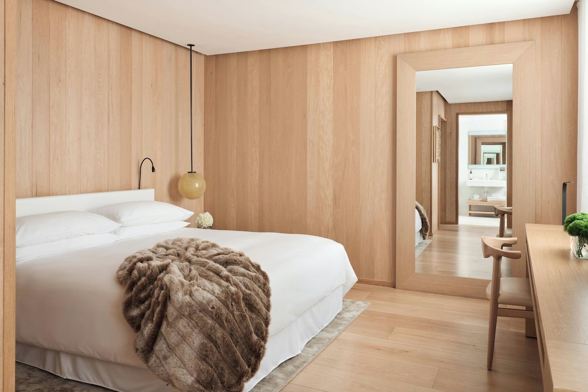 Camera da letto moderna con un letto grande, una testata in legno, una lampada da comodino e vista sul bagno.