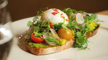 A breakfast dish with a poached egg, avocado, tomato, radish, and greens on toast, served on a white plate.