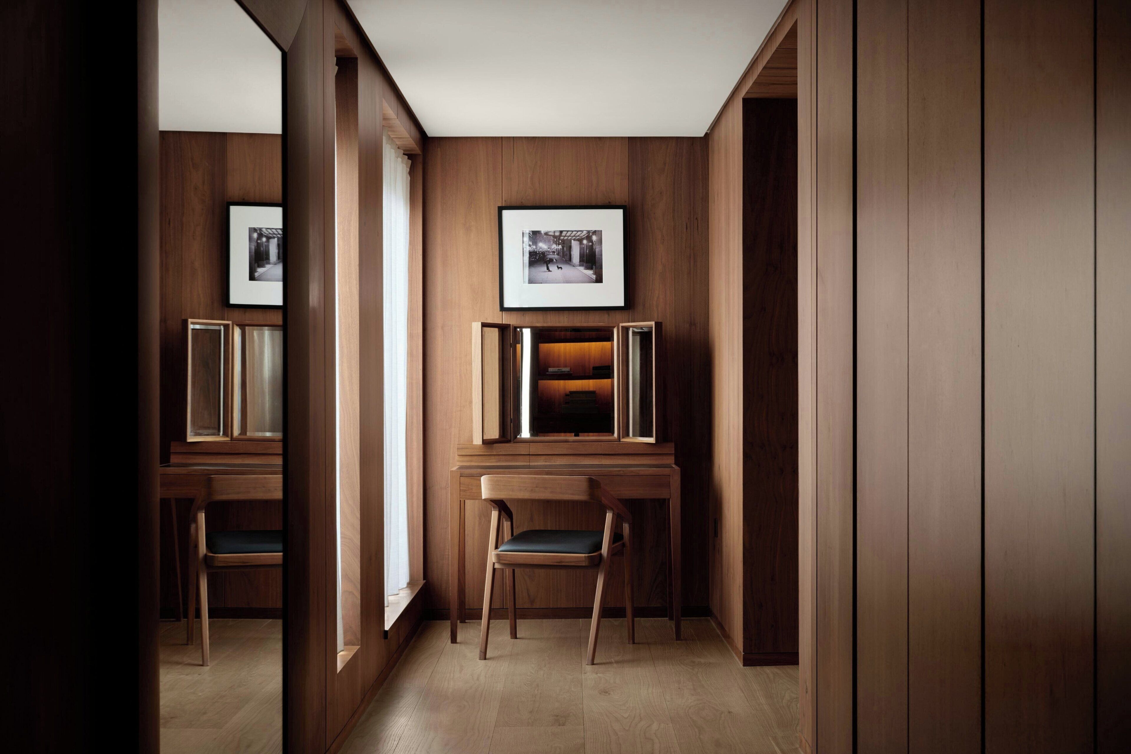 A hallway with wooden paneling, framed pictures on the walls, and a desk with a chair.