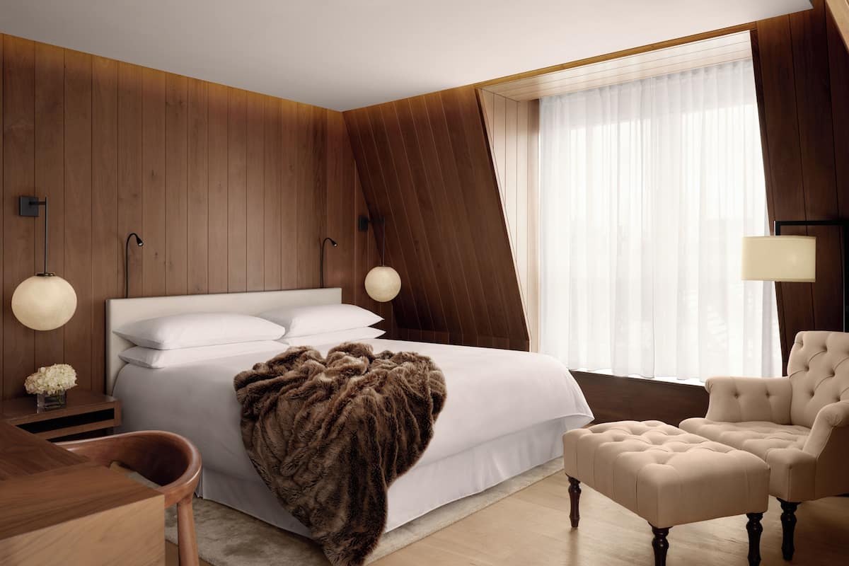 Un dormitorio con una cama, lámparas de noche, una silla y un ventanal.