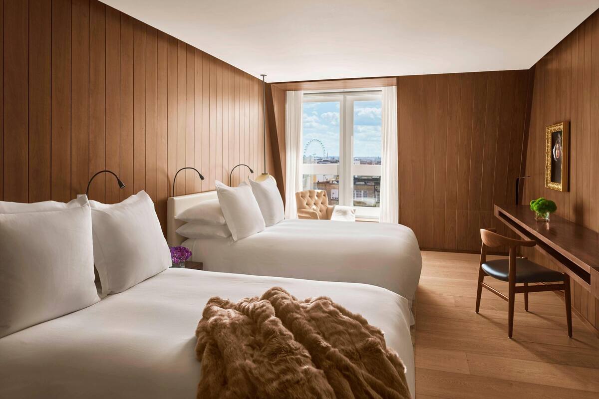 Habitación de hotel con dos camas, un escritorio y una silla. Se ve una noria a través de la ventana.