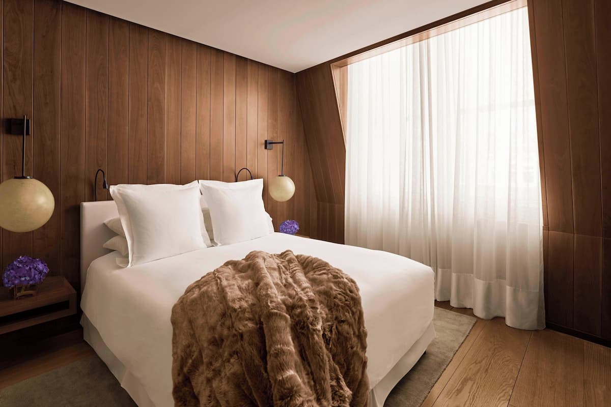 Un dormitorio con una cama grande, paneles de madera en las paredes y una ventana con cortinas traslúcidas.