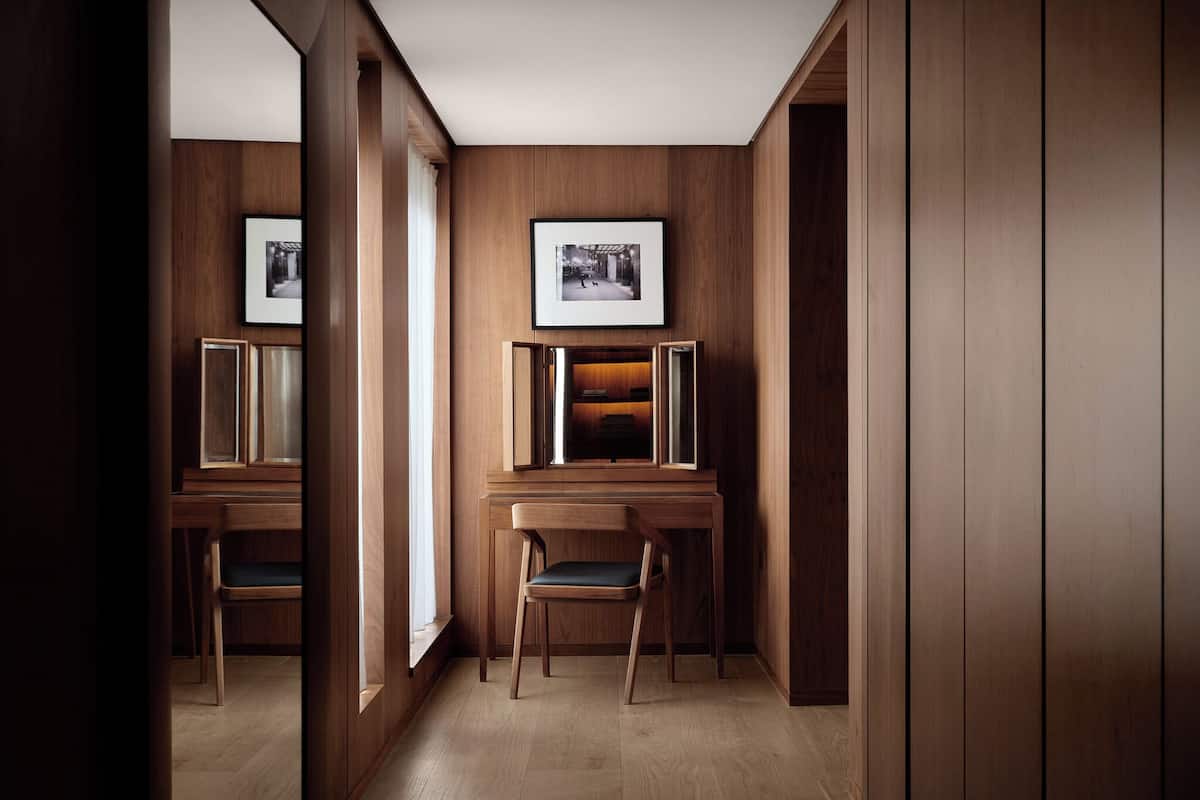 A hallway with wooden paneling, framed pictures on the walls, and a desk with a chair.