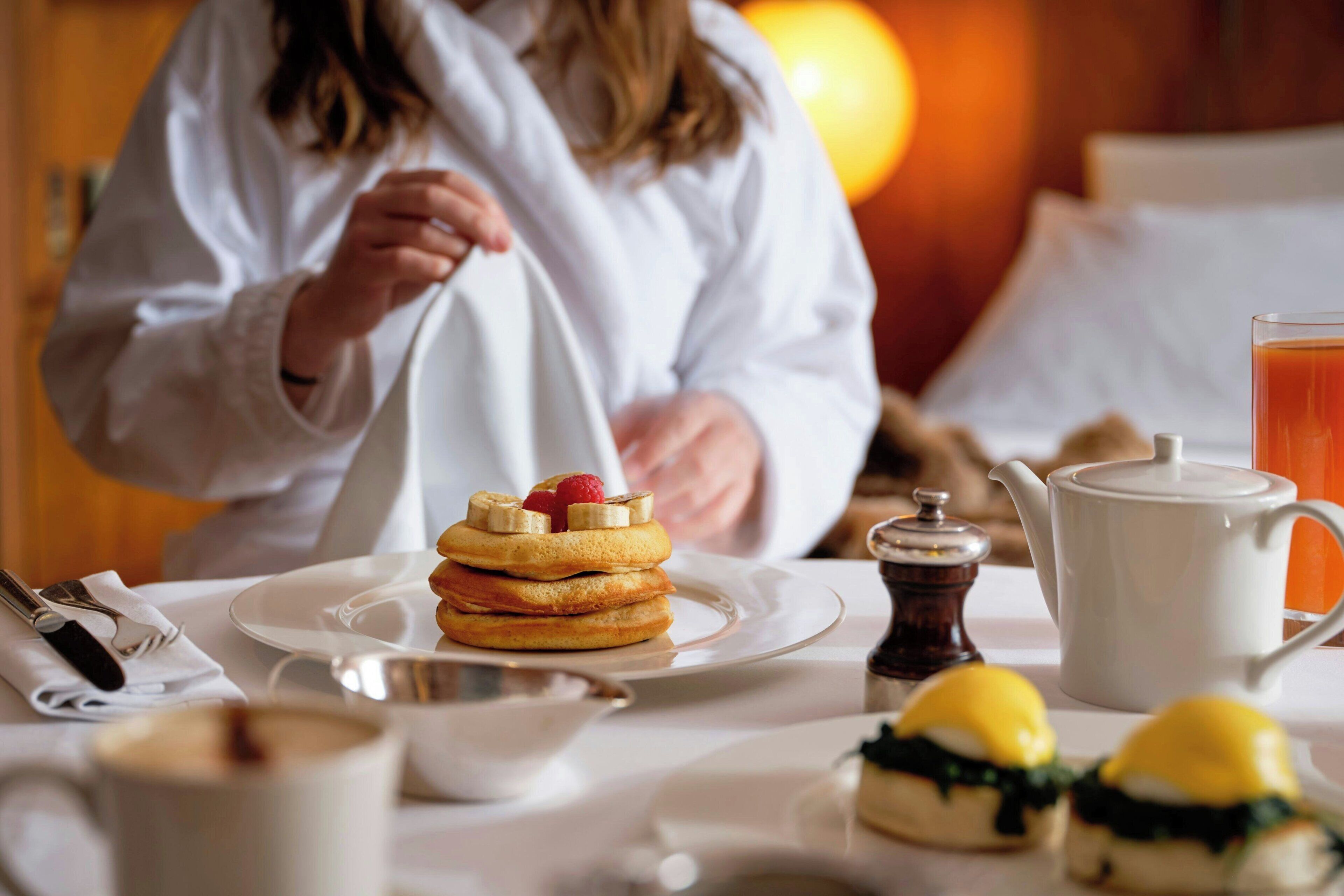 A breakfast setting with pancakes, a teapot, and a cup of tea on a table.