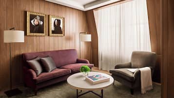 A room with a wooden paneled wall, a red sofa, a grey armchair, a round coffee table with a book and a plant, and two wall-mounted lamps.