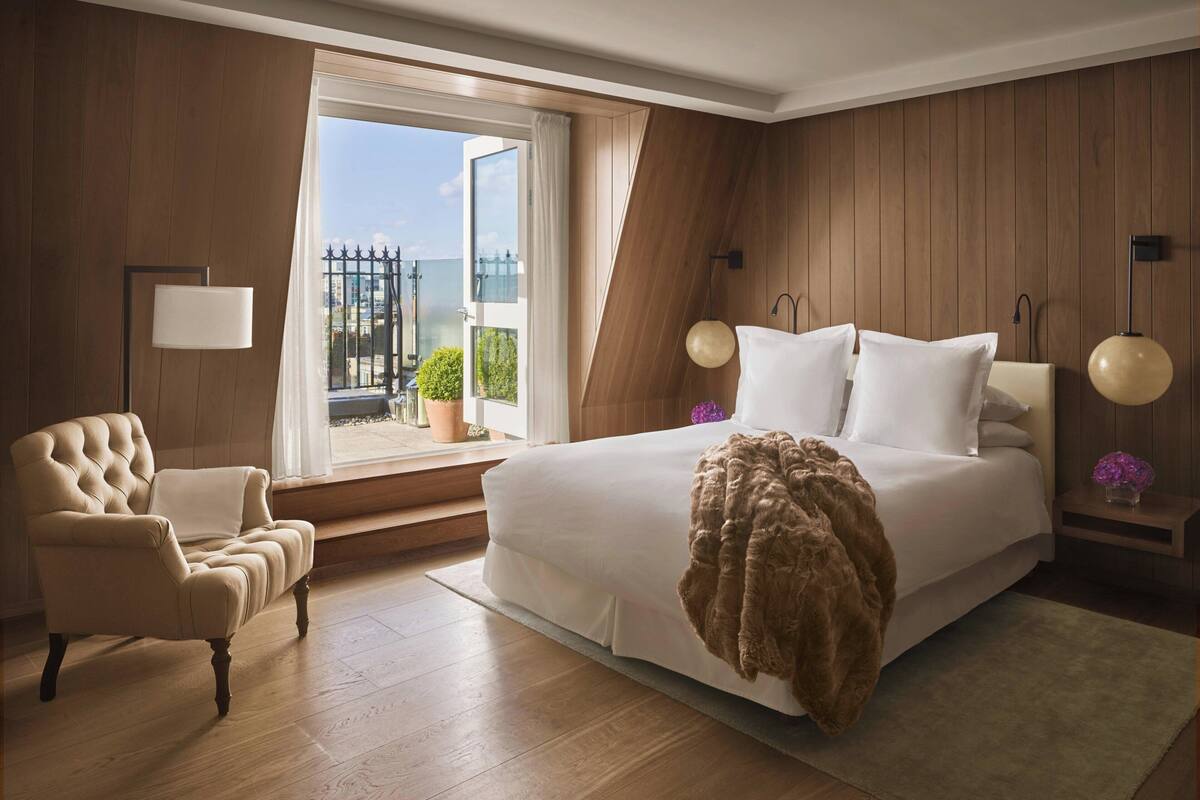 Un dormitorio con una cama grande, una silla, una mesita de noche y una ventana con vistas al exterior.
