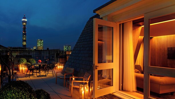 A rooftop terrace with a dining area, a sofa, and a glass door leading to a bedroom. - The London EDITION (London)