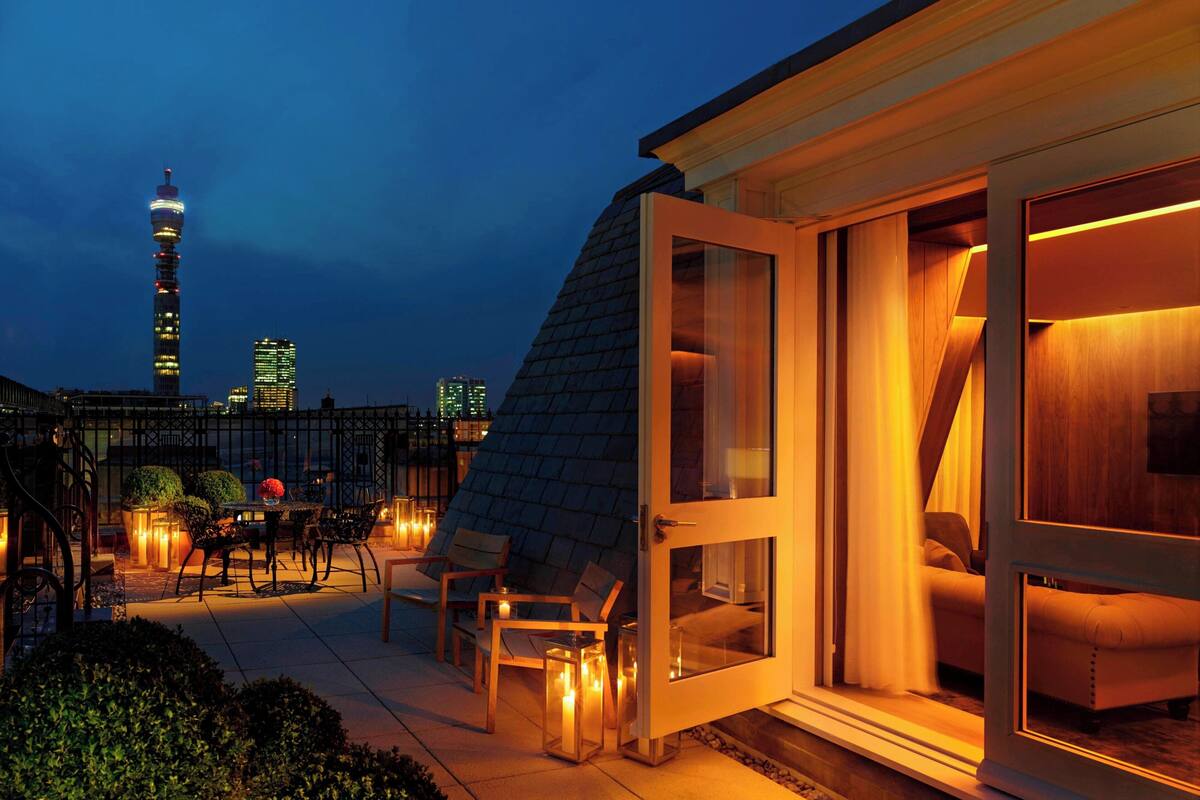 Una terraza en la azotea con zona de comedor, un sofá y una puerta de cristal que da a un dormitorio.