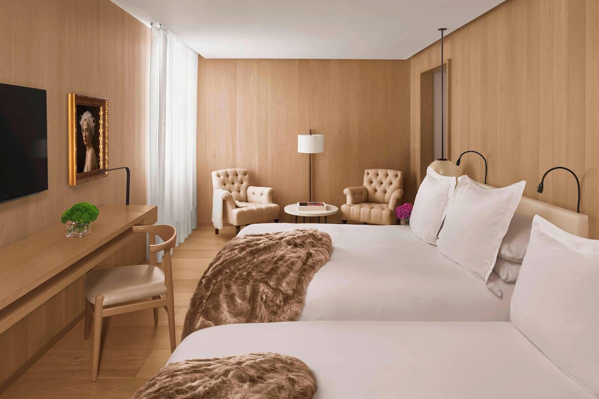 Une chambre d’hôtel avec un grand lit, deux fauteuils, une petite table ronde, un bureau avec une chaise, une télévision et une lampe.
