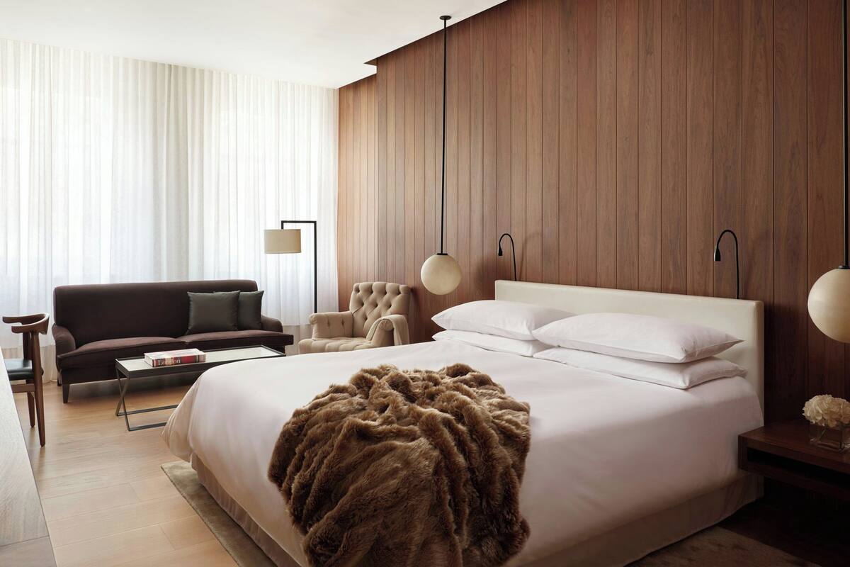 Una habitación de hotel moderna con una cama grande, un sofá, una silla y una mesita de noche con lámpara.