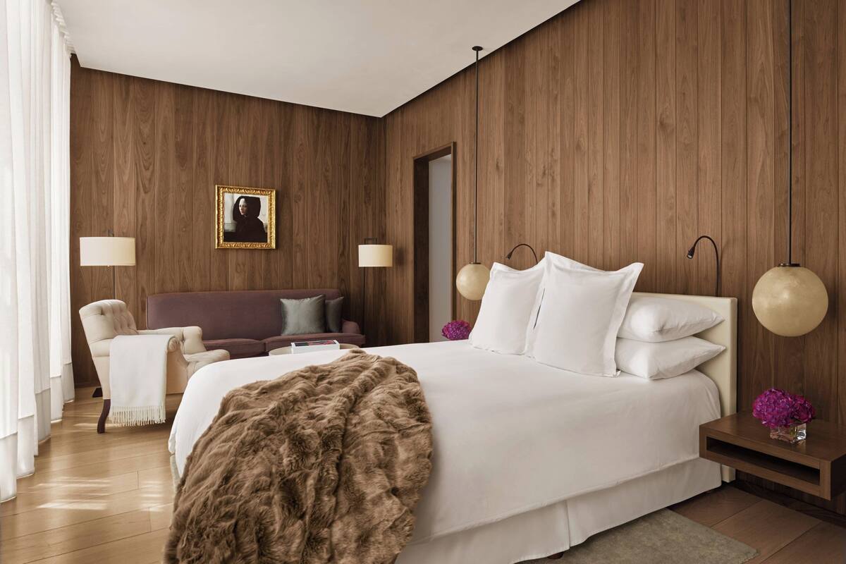 Un dormitorio moderno con una cama grande, dos mesitas de noche, un tocador, una silla, un sofá y un panel de pared de madera.