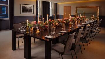 Ein langer Esstisch, festlich gedeckt für ein formelles Essen, mit Kerzen, Gläsern und floralen Tischdekorationen.
