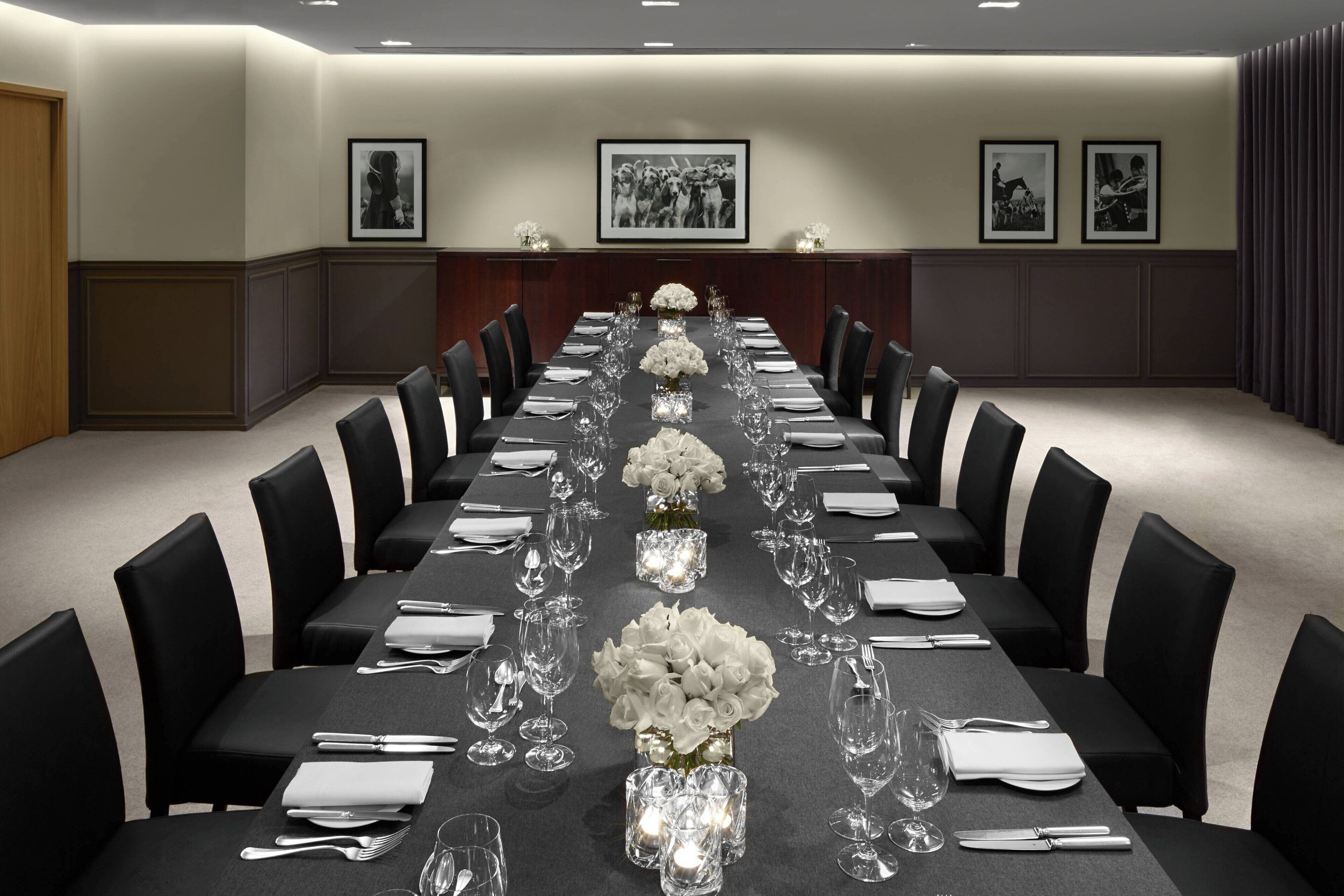 A conference room with a long table set for a formal event, flanked by chairs, with framed pictures on the walls.