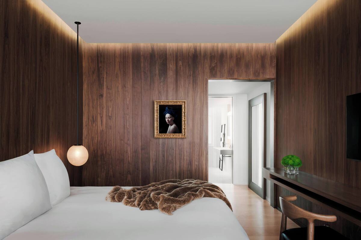 Un dormitorio moderno con un panel de madera, una cama con ropa de cama blanca, una lámpara colgante, un retrato enmarcado y una mesita de noche con una planta.
