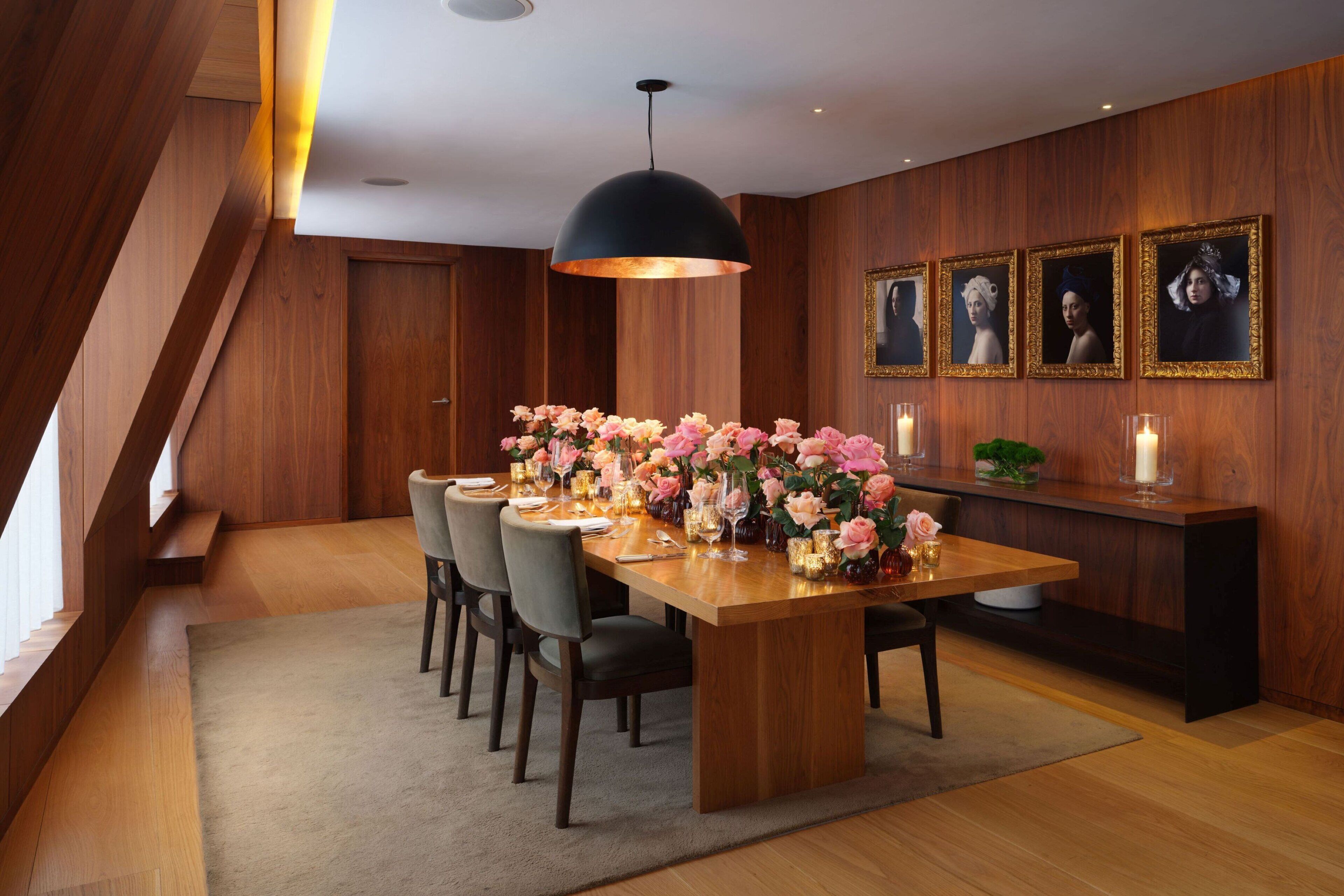 A modern dining room with a wooden table set for six, surrounded by chairs, with a large pendant light above.