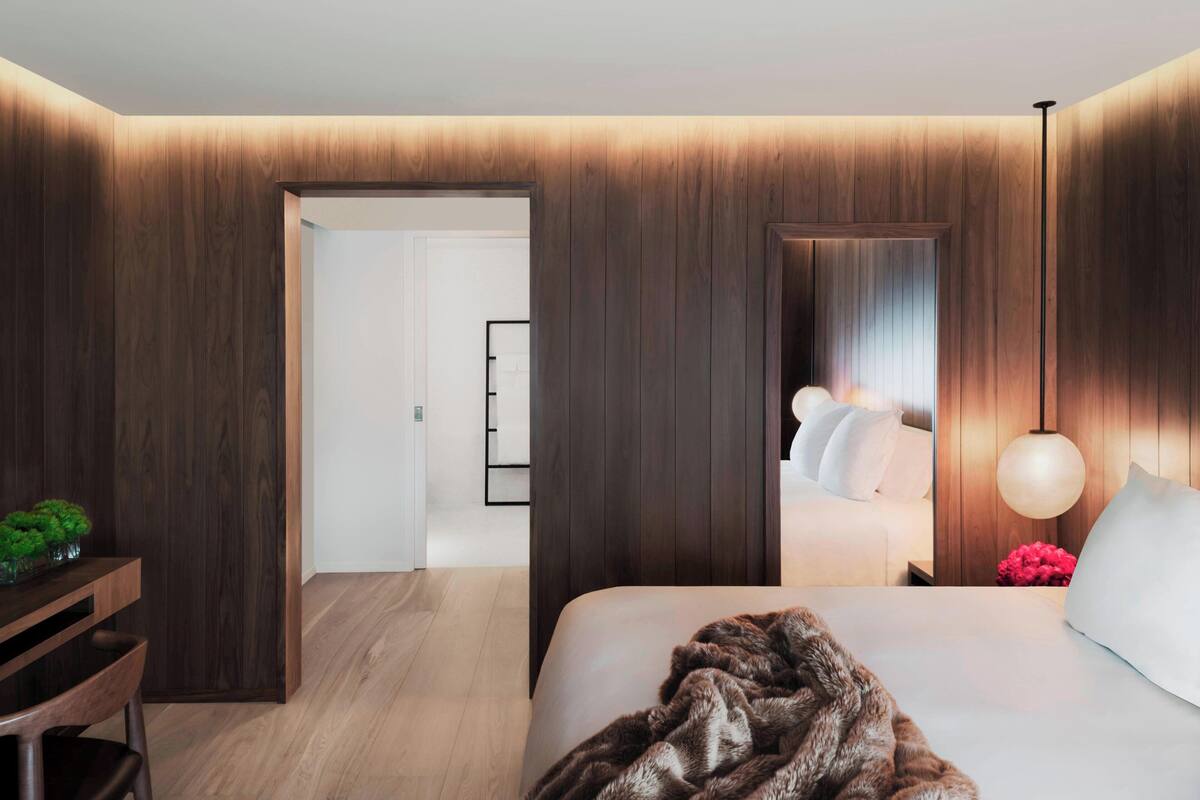 Una habitación de hotel moderna con un panel de pared de madera, una cama grande con ropa blanca, un plaid marrón mullido y una lámpara de noche.
