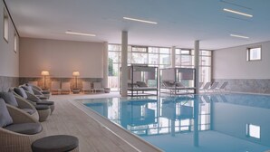 Ein Pool mit Liegestühlen und Hockern, große Fenster und ein modernes Interieur.