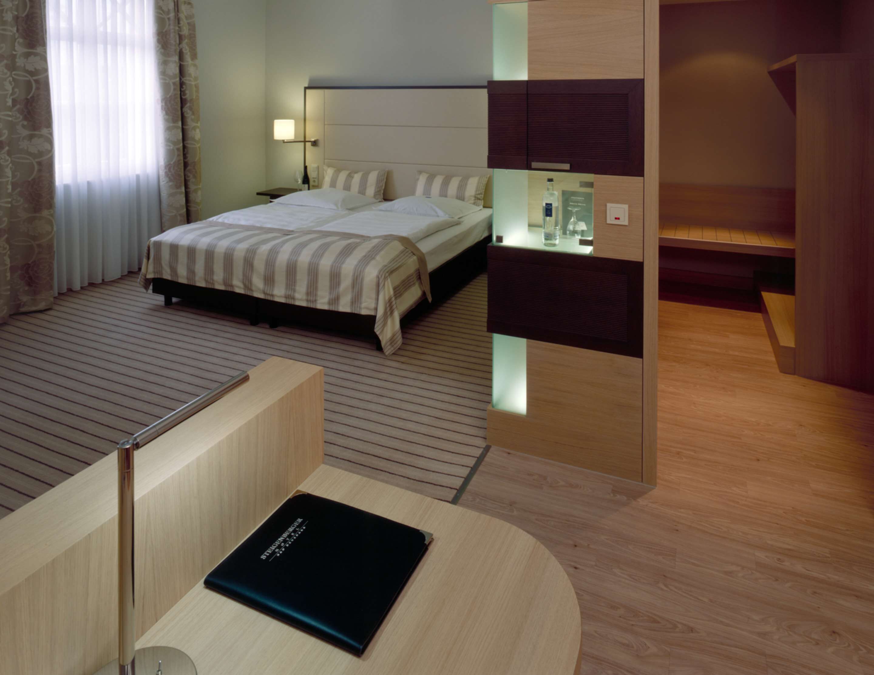A modern hotel room with a bed, bedside table, and a small desk with a chair.