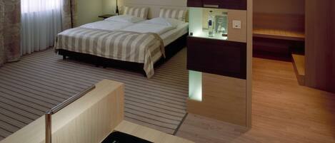 Una habitación de hotel moderna con cama, mesita de noche y un pequeño escritorio con silla.