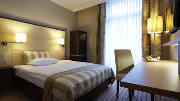 A hotel room with a bed, bedside lamps, a desk with a fruit bowl, and a mirror.
